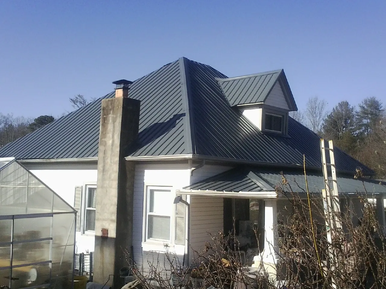 Dark blue standing seam metal roof on a white farmhouse with dormer — Slate & Tile Roof Repair by Roofing Brothers in Bluefield