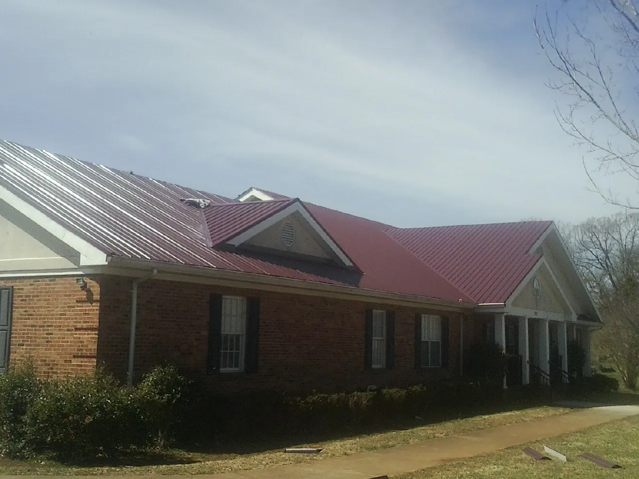 Red metal roof with gabled entries on a long brick building, from a Hail Damage Roof Repair job in Bluefield