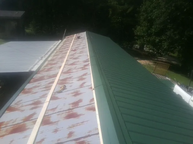 Old rusted panels beside newly installed green metal roofing — Wind Damage Roof Repair by Roofing Brothers in Bluefield