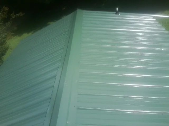 New green metal panels meeting at the ridge of a roof — Flat Roof Repair work by our crew in Bluefield