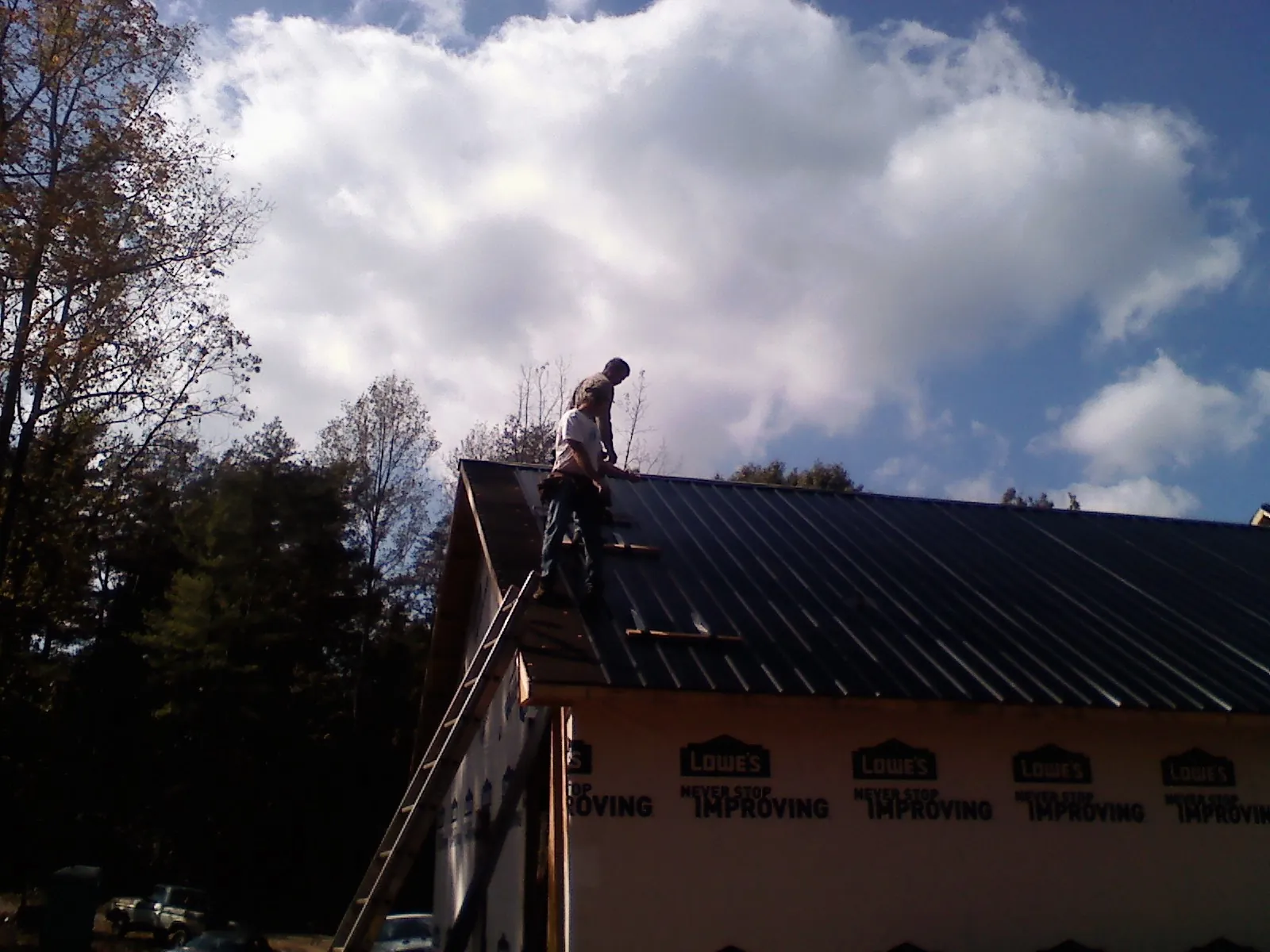 Roofer fastening dark metal panels high against a cloudy sky, from a Roof Inspection job in Bluefield