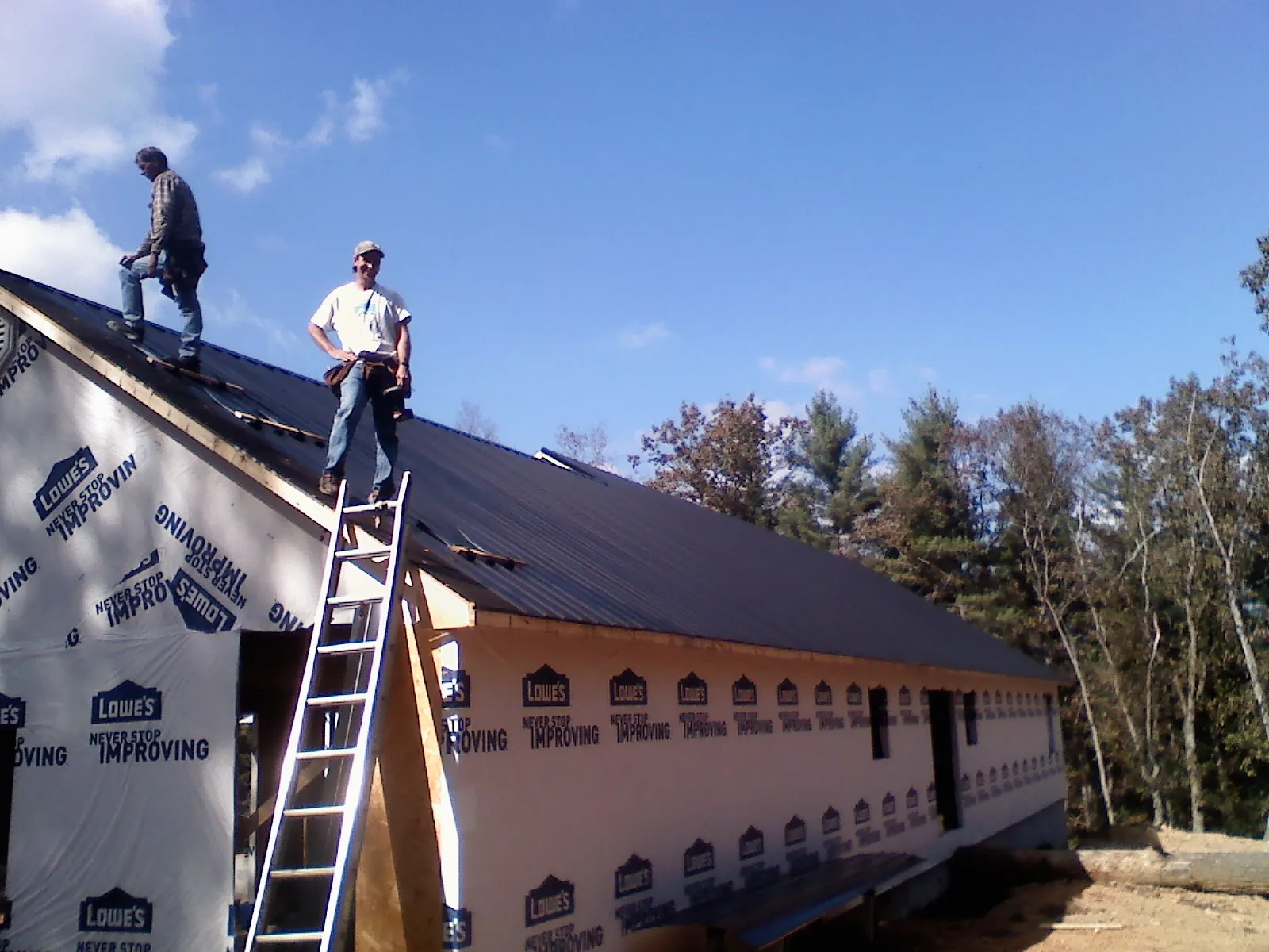 Two roofers standing on a long dark metal roof over a wrapped building in Bluefield