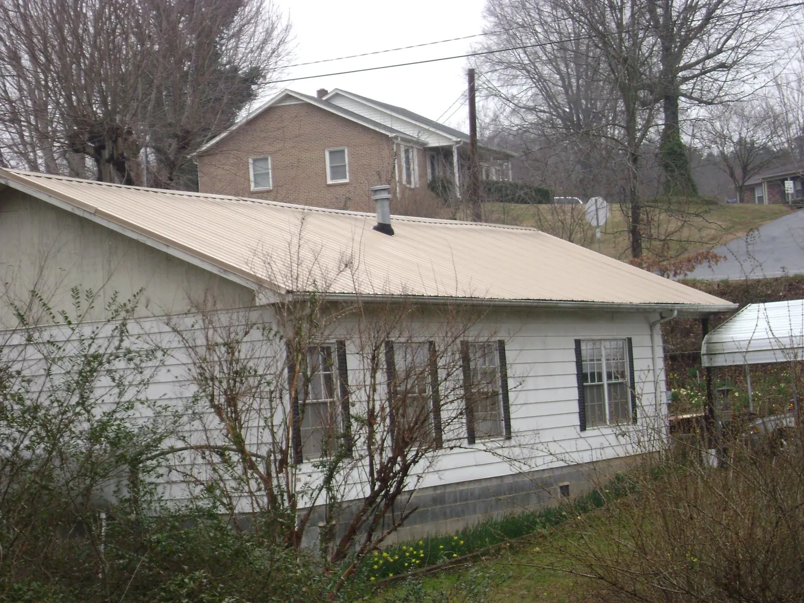 Tan metal roof on a white sided house set into a hillside — Commercial Roofing by Roofing Brothers in Bluefield